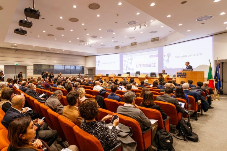 Sala conferenze piena durante l’Innovation Day Lazio Life Science, con il pubblico seduto e un relatore al podio.